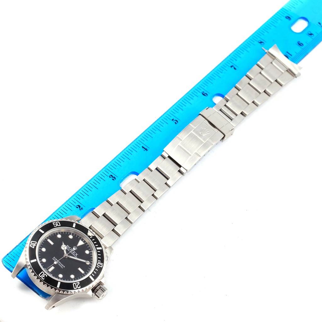 The image shows a top view of a Rolex Submariner 14060 Men's Stainless Steel Black Dial 14060 Men's Stainless Steel Black Dial watch with its strap extended alongside a blue ruler.