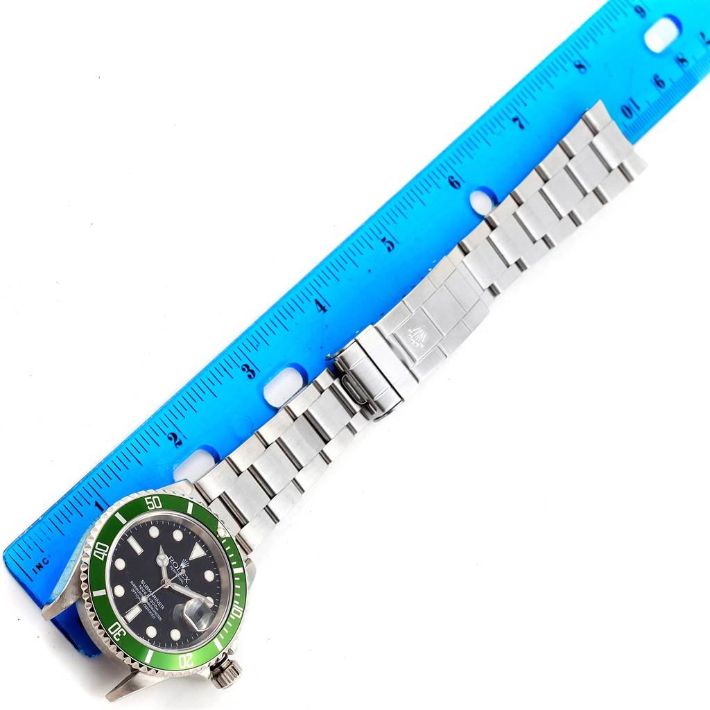 The image shows the Rolex Submariner 16610LV Men's Stainless Steel Black Dial 16610LV Men's Stainless Steel Black Dial watch from a top view, including its green bezel, dial, and bracelet next to a blue ruler for scale.