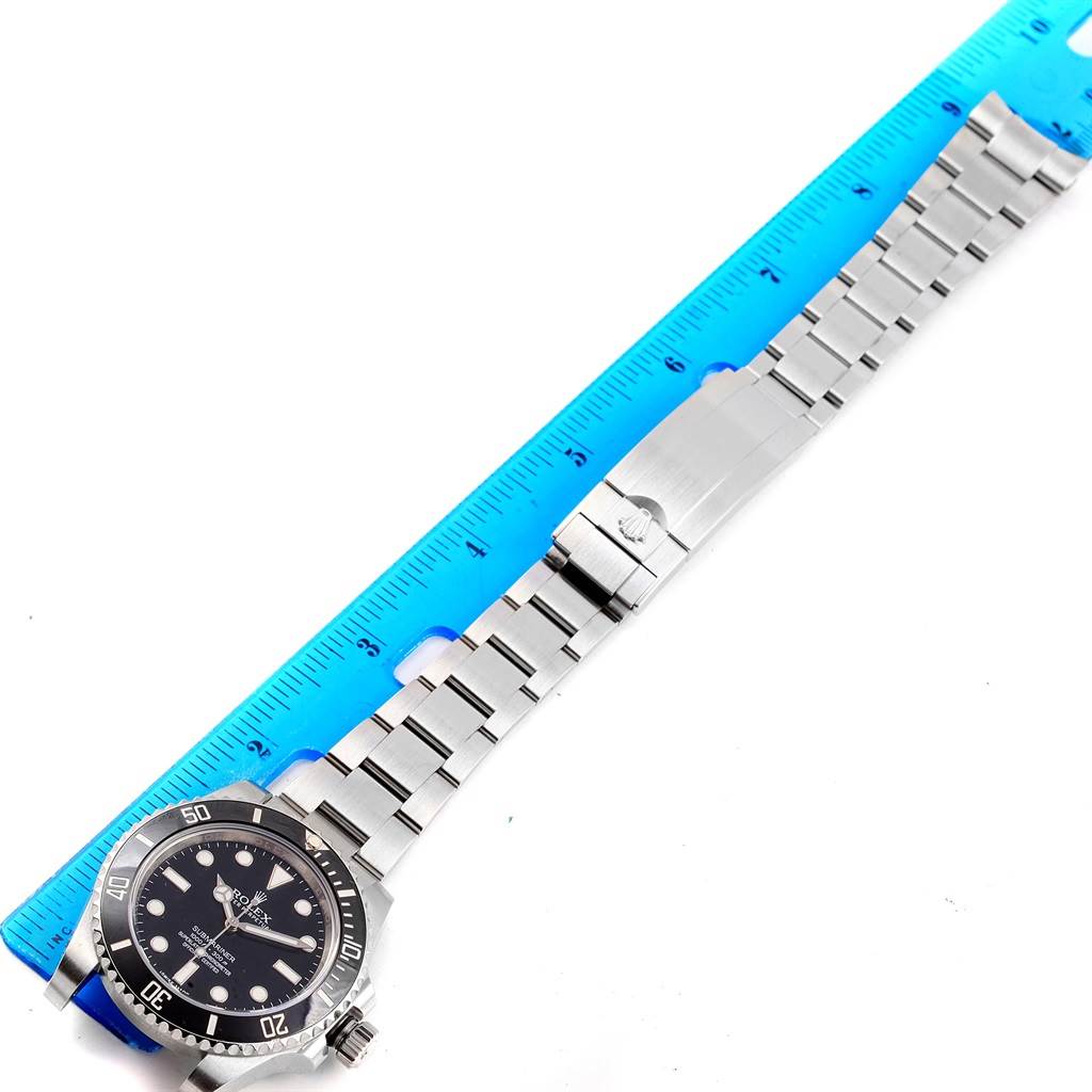 The Rolex Submariner 114060 Men's Stainless Steel Black Dial 114060 Men's Stainless Steel Black Dial watch is shown laid flat, highlighting its dial, bezel, and full metal bracelet with a reference ruler.