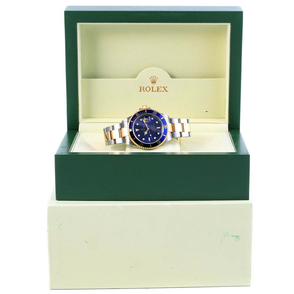 The Rolex Submariner 16613 Men's Steel and Gold (two tone) Blue Dial 16613 Men's Steel and Gold (two tone) Blue Dial watch is presented inside its green and beige Rolex-branded box, showing the face and bracelet.