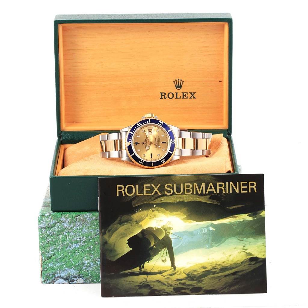 The Rolex Submariner 16613 Men's Steel and Gold (two tone) Champagne Dial 16613 Men's Steel and Gold (two tone) Champagne Dial watch is shown front-on, inside its box, with a booklet in front.