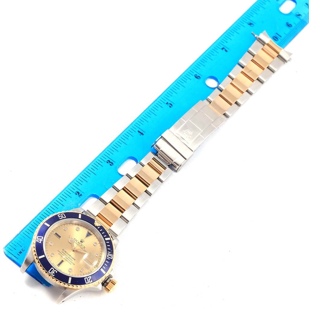This image shows a Rolex Submariner 16613 Men's Steel and Gold (two tone) Champagne Dial 16613 Men's Steel and Gold (two tone) Champagne Dial watch laid flat with a blue ruler measuring its length.