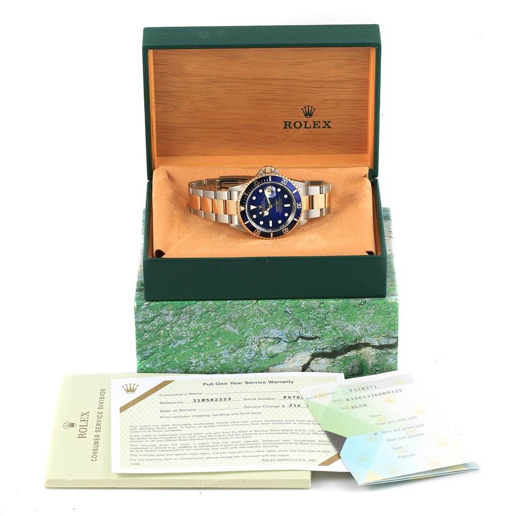 The Rolex Submariner 16613 Men's Steel and Gold (two tone) Blue Dial 16613 Men's Steel and Gold (two tone) Blue Dial watch is displayed from the front inside its open box with documentation in front.