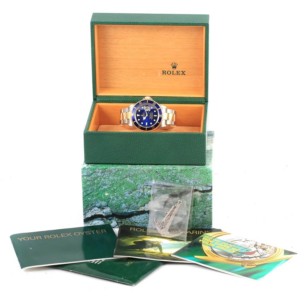 The Rolex Submariner 16613 Men's Steel and Gold (two tone) Blue Dial 16613 Men's Steel and Gold (two tone) Blue Dial watch is displayed frontally in an open green box with booklets and accessories in front.