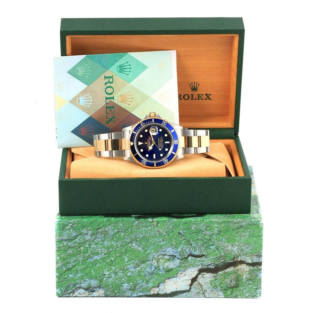This image shows a front view of a Rolex Submariner 16613 Men's Steel and Gold (two tone) Blue Dial 16613 Men's Steel and Gold (two tone) Blue Dial watch in its green box with an instruction booklet.