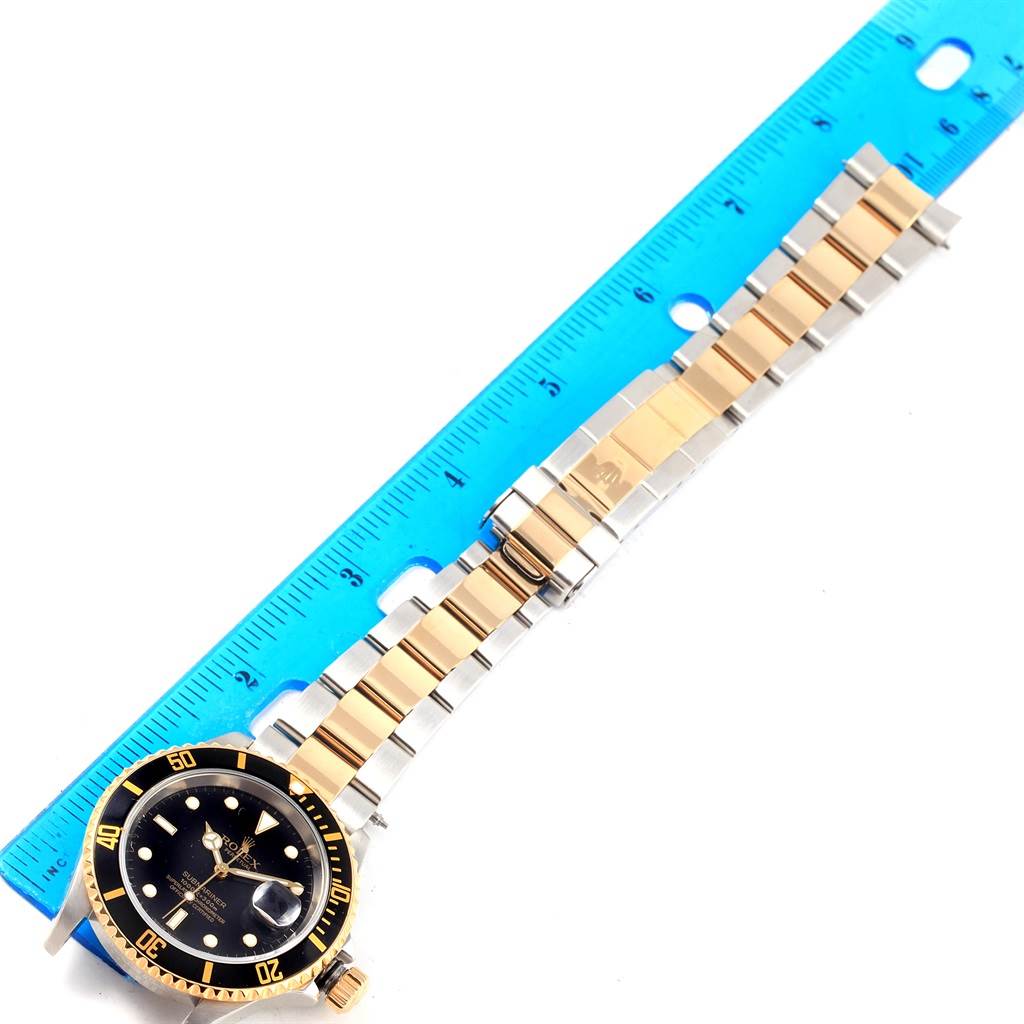 The image shows a top-down view of a Rolex Submariner 16613 Men's Steel and Gold (two tone) Black Dial 16613 Men's Steel and Gold (two tone) Black Dial watch, including its face, bezel, and bracelet, alongside a blue ruler.