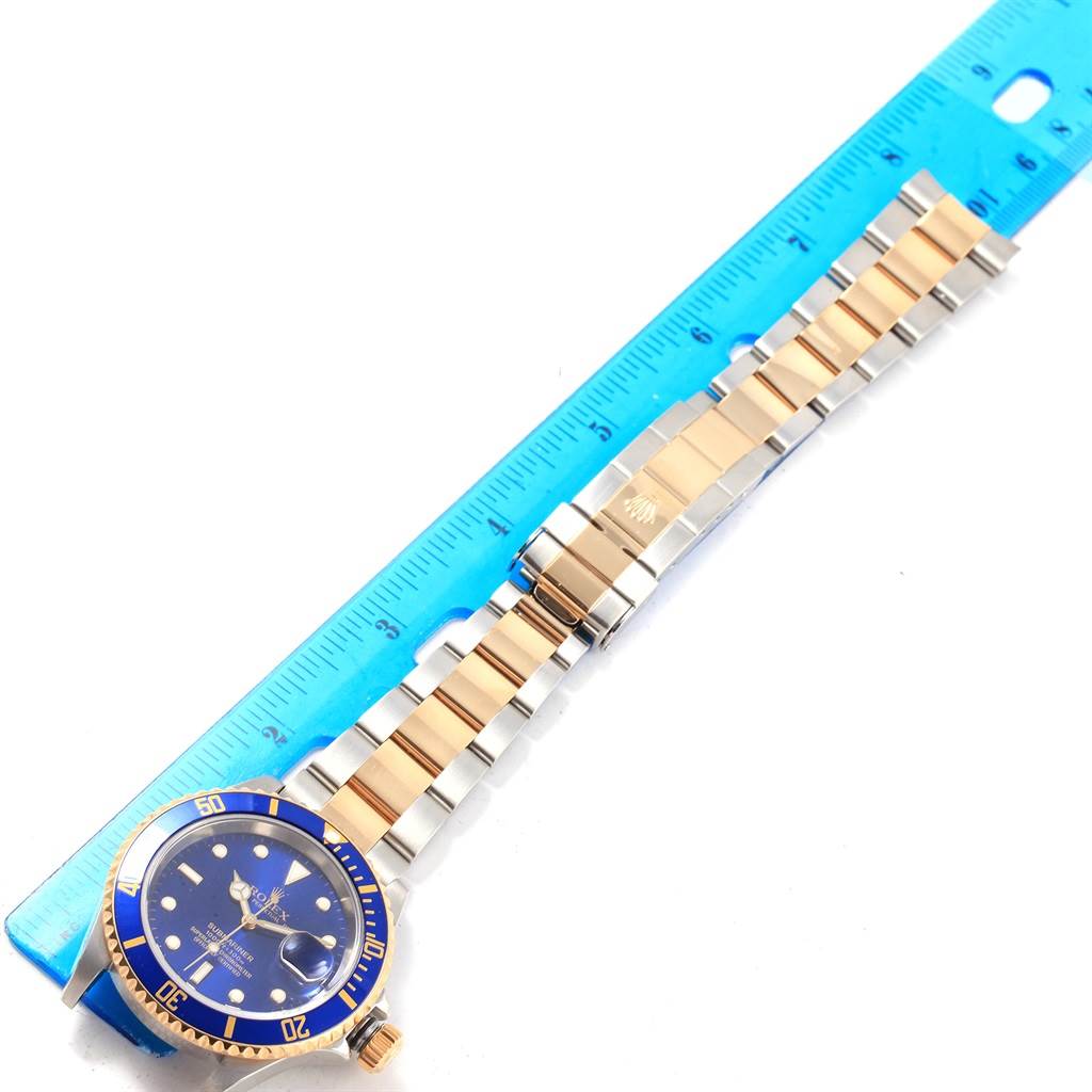 The image shows a top view of a Rolex Submariner 16613 Men's Steel and Gold (two tone) Blue Dial 16613 Men's Steel and Gold (two tone) Blue Dial watch with a blue dial, gold accents, and a measured bracelet laid next to a ruler.