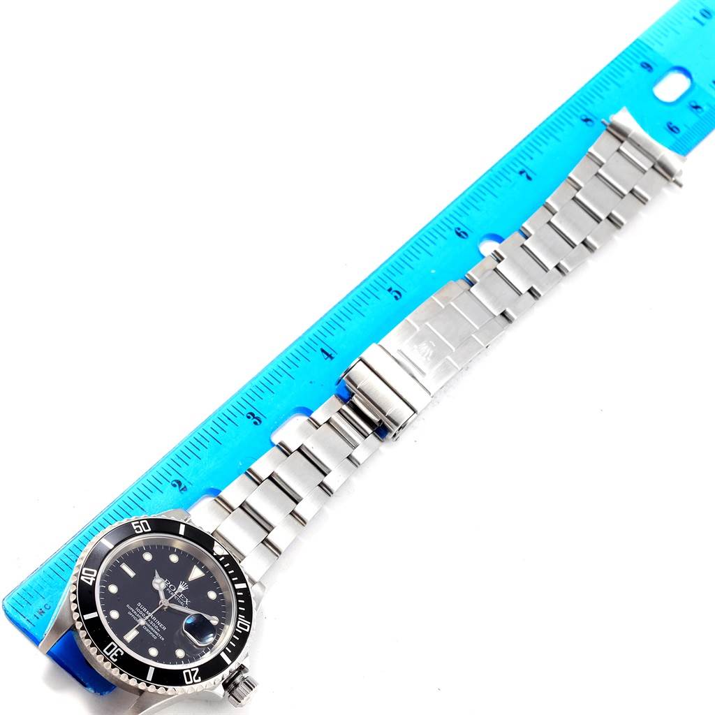 The image shows a top-down view of a Rolex Submariner 16610 Men's Stainless Steel Black Dial 16610 Men's Stainless Steel Black Dial watch, including its face and bracelet, alongside a blue ruler.