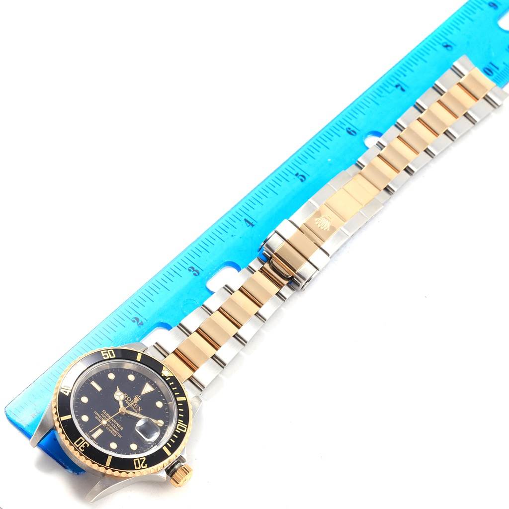 The Rolex Submariner 16613 Men's Steel and Gold (two tone) Black Dial 16613 Men's Steel and Gold (two tone) Black Dial watch is shown from a top-down angle, featuring the dial, bezel, and bracelet with a ruler for scale.