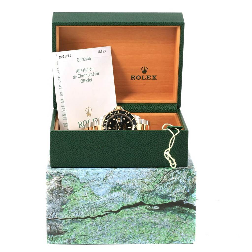 The image shows a Rolex Submariner 16613 Men's Steel and Gold (two tone) Black Dial 16613 Men's Steel and Gold (two tone) Black Dial watch in its open green box, accompanied by an official warranty document.