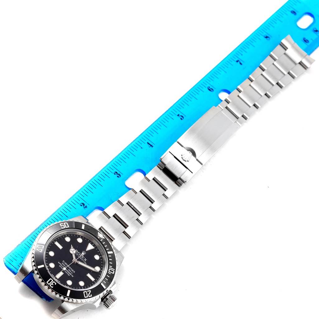 The image shows a full view of the Rolex Submariner 114060 Men's Stainless Steel Black Dial 114060 Men's Stainless Steel Black Dial, including its face, bezel, and metal band, positioned next to a blue ruler.