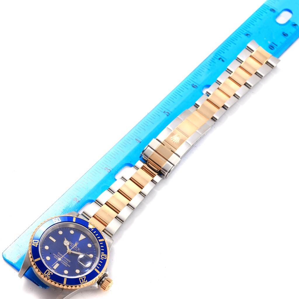 The Rolex Submariner 16613 Men's Steel and Gold (two tone) Blue Dial 16613 Men's Steel and Gold (two tone) Blue Dial watch is shown from a top-down angle, displaying the face, bezel, and full bracelet next to a ruler.