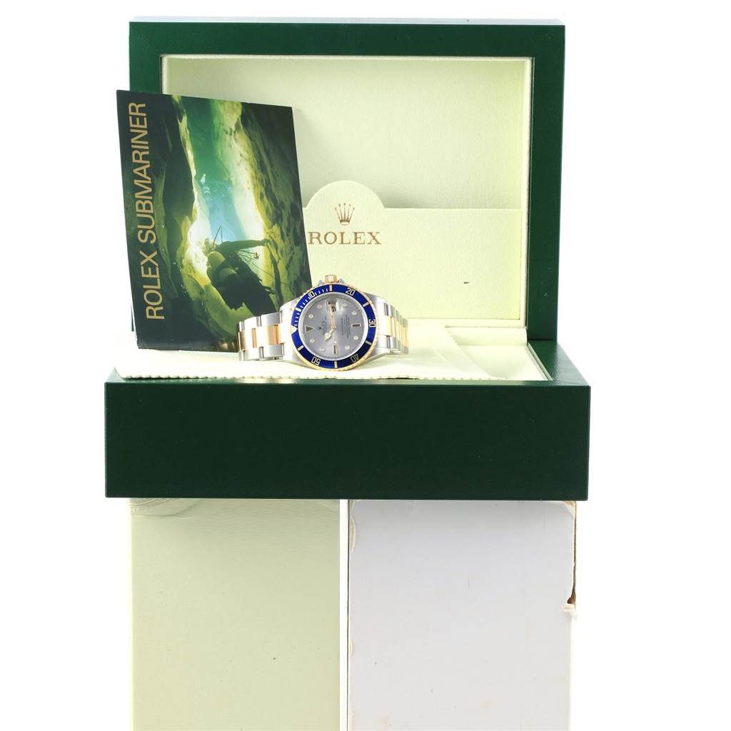 The Rolex Submariner 16613 Men's Steel and Gold (two tone) Grey Dial 16613 Men's Steel and Gold (two tone) Grey Dial watch is displayed front-facing in an open green box, accompanied by a booklet.
