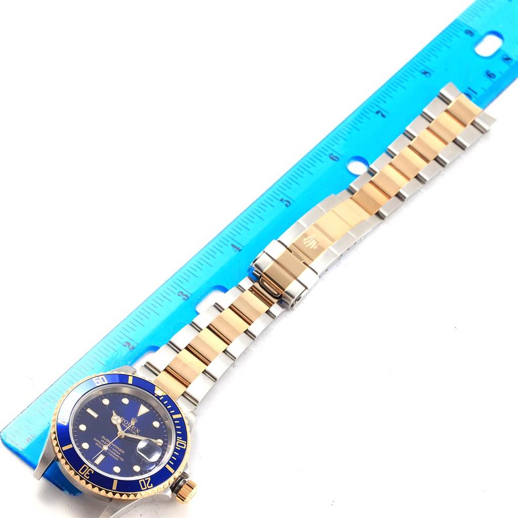 The Rolex Submariner 16613 Men's Steel and Gold (two tone) Blue Dial 16613 Men's Steel and Gold (two tone) Blue Dial watch, angled flat, shows the face, bezel, crown, and entire band next to a blue ruler for scale.