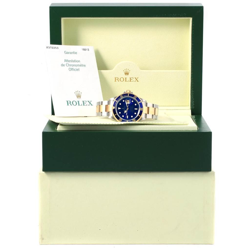 This image shows a Rolex Submariner 16613 Men's Steel and Gold (two tone) Blue Dial 16613 Men's Steel and Gold (two tone) Blue Dial watch in its open box with a warranty card beside it.