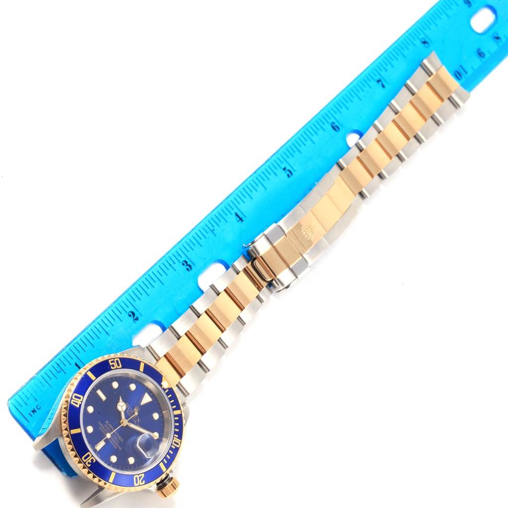 This image shows a Rolex Submariner 16613 Men's Steel and Gold (two tone) Blue Dial 16613 Men's Steel and Gold (two tone) Blue Dial watch laid flat alongside a ruler, displaying the face, bezel, and bracelet.