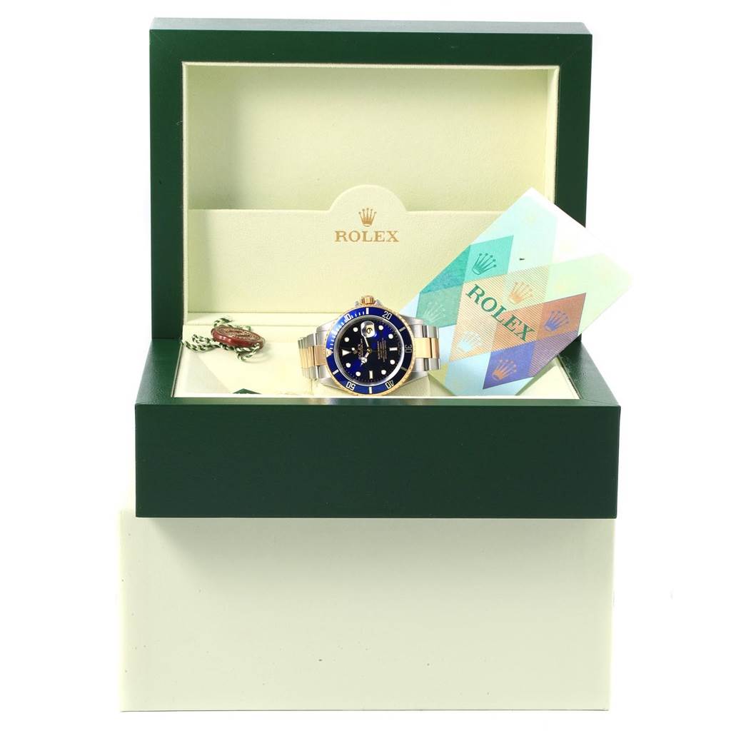 The image shows a Rolex Submariner 16613 Men's Steel and Gold (two tone) Blue Dial 16613 Men's Steel and Gold (two tone) Blue Dial watch positioned in its open presentation box with accompanying warranty cards.