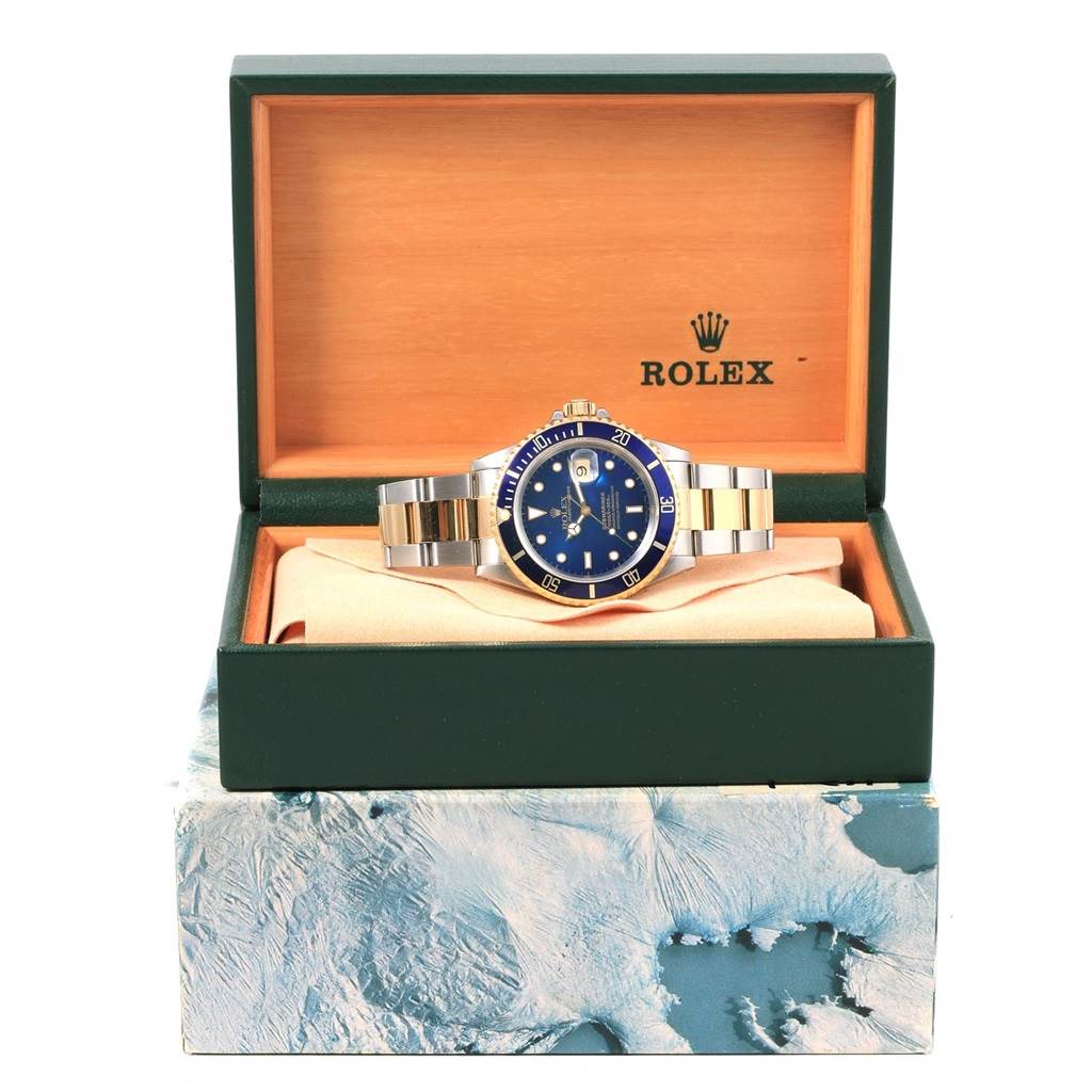 The Rolex Submariner 16613 Men's Steel and Gold (two tone) Blue Dial 16613 Men's Steel and Gold (two tone) Blue Dial watch is shown from the front, placed inside an open green and wooden box.