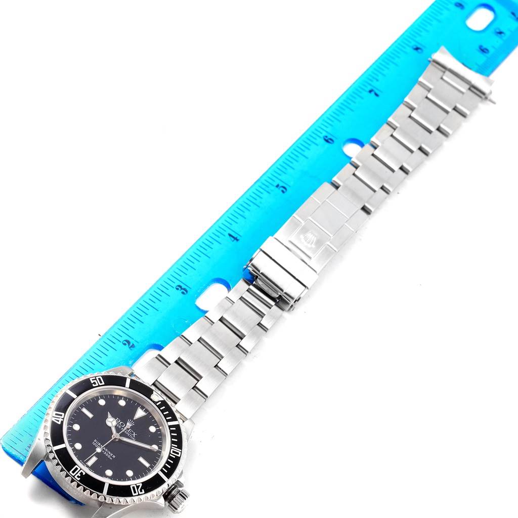 The image shows a Rolex Submariner 14060 Men's Stainless Steel Black Dial 14060 Men's Stainless Steel Black Dial watch laid flat next to a ruler, highlighting its dial, bezel, and stainless steel bracelet.