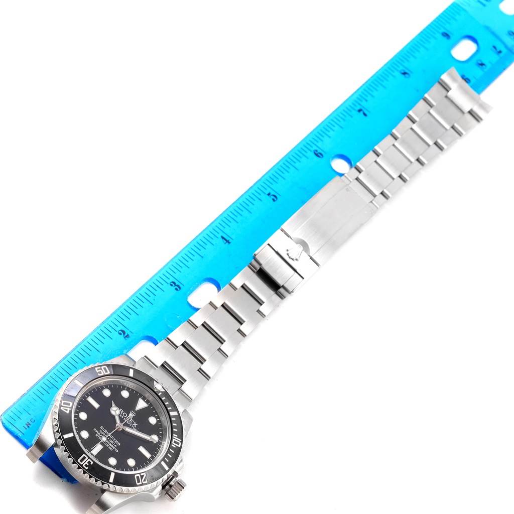 The image shows a Rolex Submariner 114060 Men's Stainless Steel Black Dial 114060 Men's Stainless Steel Black Dial watch at an overhead angle, alongside a blue measuring ruler.