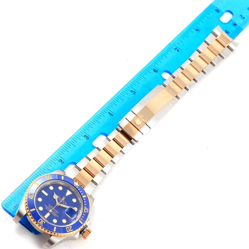 The image shows a Rolex Submariner 116613 Men's Steel and Gold (two tone) Blue Dial 116613 Men's Steel and Gold (two tone) Blue Dial watch laid flat beside a blue ruler, highlighting its bracelet and face.
