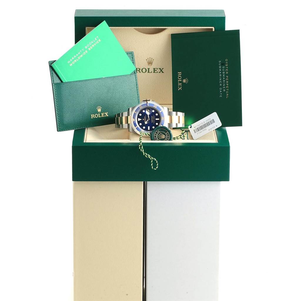 The Rolex Submariner 116613 Men's Steel and Gold (two tone) Blue Dial 116613 Men's Steel and Gold (two tone) Blue Dial watch is shown from the front in its box, alongside warranty booklets and packaging accessories.