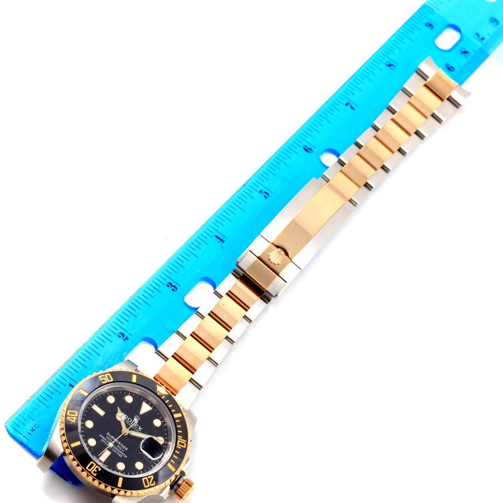 The image shows a Rolex Submariner 116613 Men's Steel and Gold (two tone) Black Dial 116613 Men's Steel and Gold (two tone) Black Dial watch positioned next to a ruler, displaying its full face and bracelet.