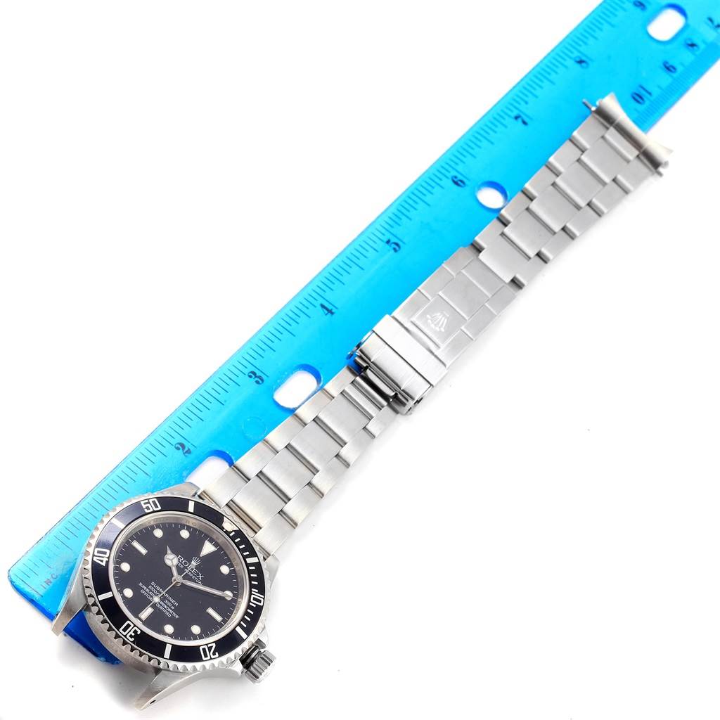 The image displays a Rolex Submariner 14060 Men
s Stainless Steel Black Dial 14060 Men
s Stainless Steel Black Dial watch laid flat, with the dial, bezel, and bracelet visible next to a ruler for measurement.