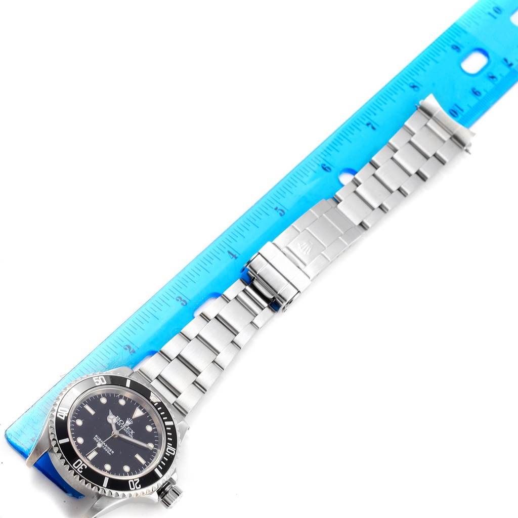 This image shows a top-down view of a Rolex Submariner 14060 Men's Stainless Steel Black Dial 14060 Men's Stainless Steel Black Dial watch alongside a blue ruler for scale.