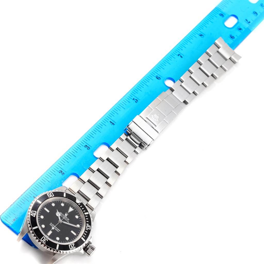 The Rolex Submariner 14060 Men's Stainless Steel Black Dial 14060 Men's Stainless Steel Black Dial watch is shown laid flat next to a ruler, displaying the face, bezel, bracelet, and clasp.