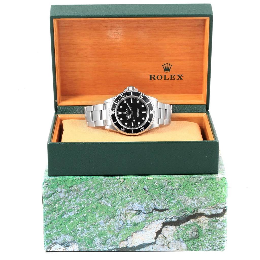 The Rolex Submariner 14060 Men's Stainless Steel Black Dial 14060 Men's Stainless Steel Black Dial watch is shown from a front angle inside an open green and wood box with its bracelet spread out.