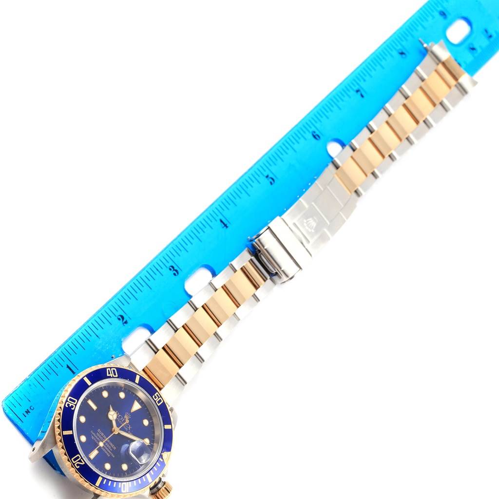 The image shows a Rolex Submariner 16613 Men's Steel and Gold (two tone) Blue Dial 16613 Men's Steel and Gold (two tone) Blue Dial watch laid flat next to a ruler, displaying the entire watch and its band.