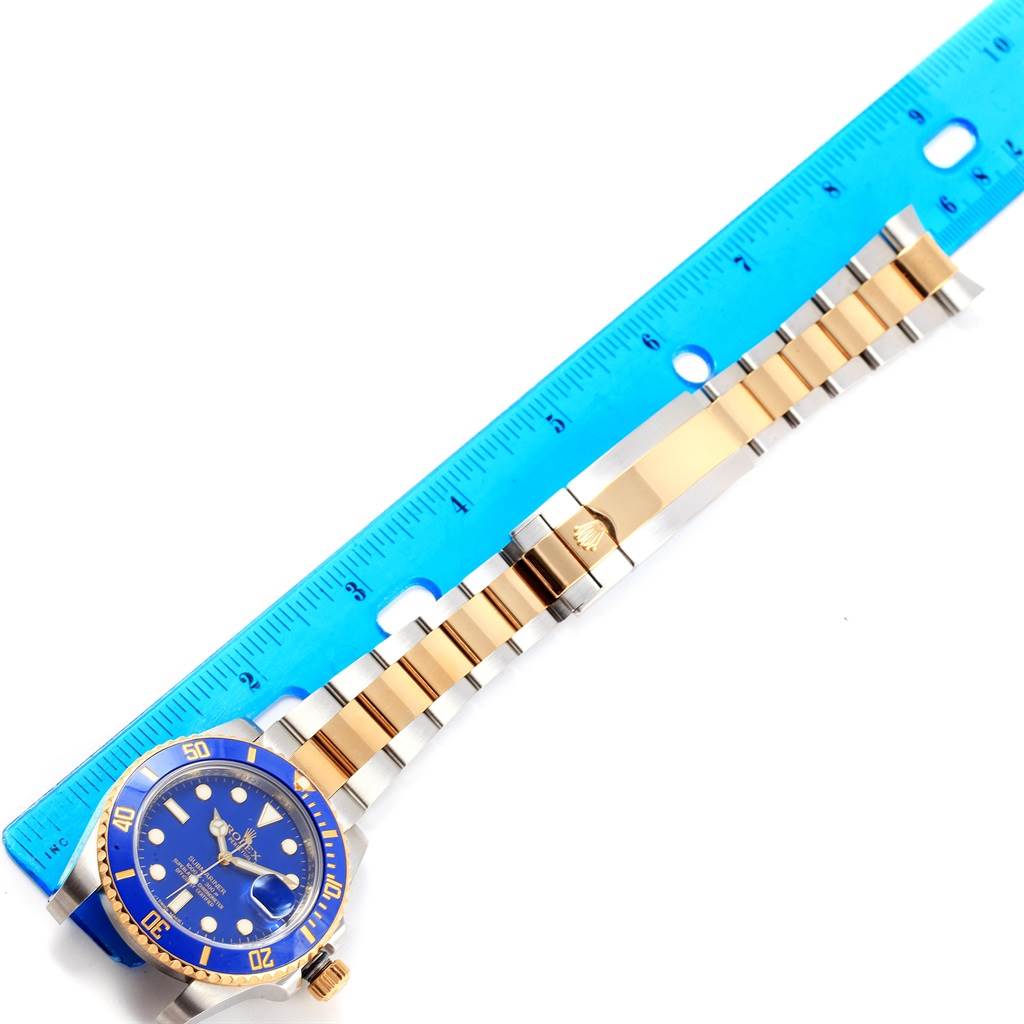 The image shows a Rolex Submariner 116613 Men's Steel and Gold (two tone) Blue Dial 116613 Men's Steel and Gold (two tone) Blue Dial watch with a blue dial and two-tone bracelet, positioned next to a blue ruler.