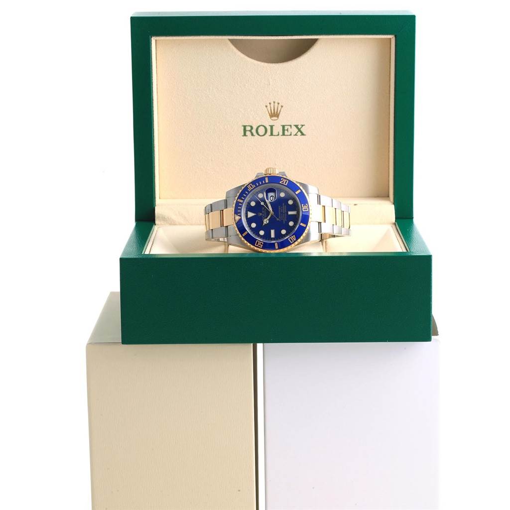 The Rolex Submariner 116613 Men's Steel and Gold (two tone) Blue Dial 116613 Men's Steel and Gold (two tone) Blue Dial watch is displayed frontally in an open green box, showing the blue dial, bezel, and bracelet.