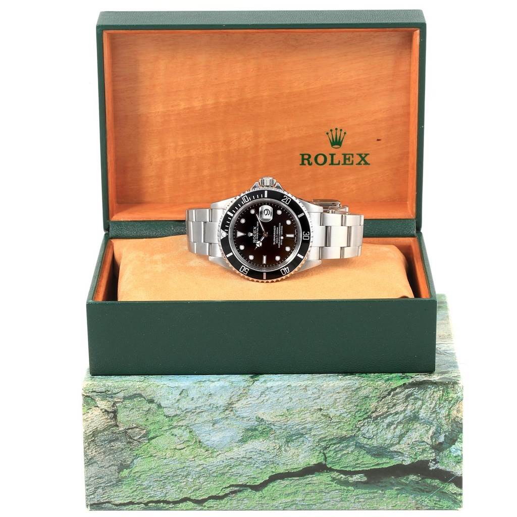 The Rolex Submariner 16610 Men's Stainless Steel Black Dial 16610 Men's Stainless Steel Black Dial watch is shown at a front angle inside an open green and wood Rolex box.