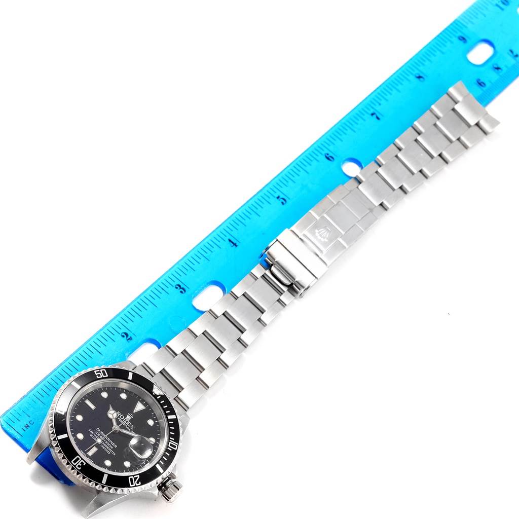 The image shows a Rolex Submariner 16610 Men's Stainless Steel Black Dial 16610 Men's Stainless Steel Black Dial watch, angled flat, with its bracelet and clasp extended alongside a ruler.