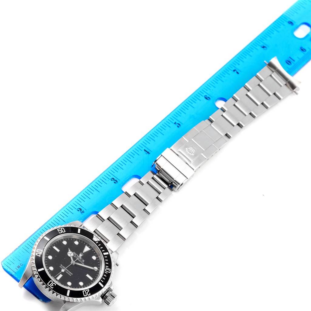 The Rolex Submariner 14060 Men's Stainless Steel Black Dial 14060 Men's Stainless Steel Black Dial watch is shown from an overhead angle with its strap extended alongside a blue ruler.