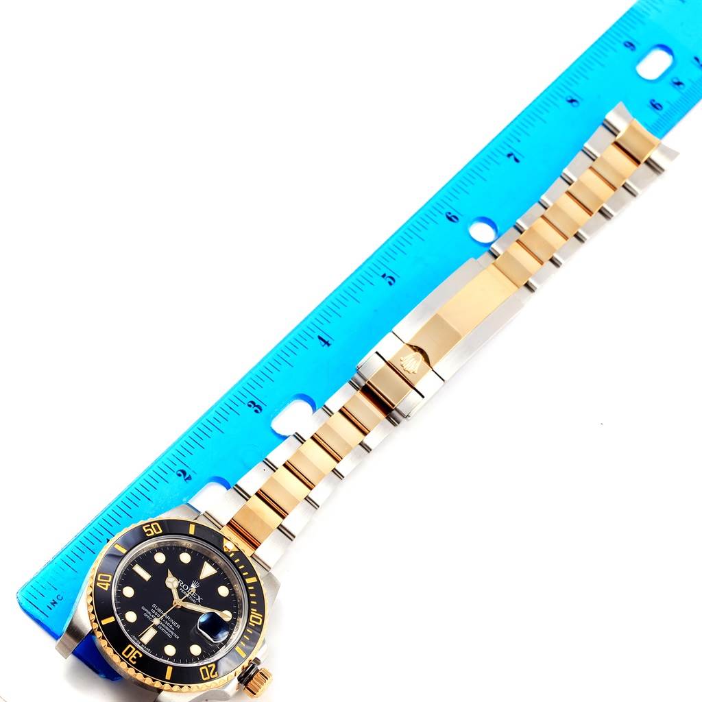 The Rolex Submariner 116613 Men's Steel and Gold (two tone) Black Dial 116613 Men's Steel and Gold (two tone) Black Dial watch is shown from an overhead angle, displaying its face, bezel, and two-tone bracelet alongside a ruler for scale.