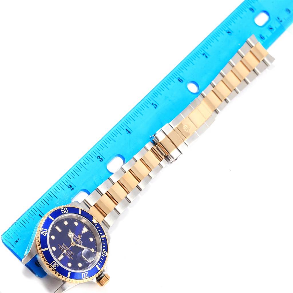 The image shows a Rolex Submariner 16613 Steel and Gold (two tone) Blue Dial 16613 Steel and Gold (two tone) Blue Dial watch positioned diagonally, with its bezel, face, and bracelet visible alongside a blue ruler for scale.