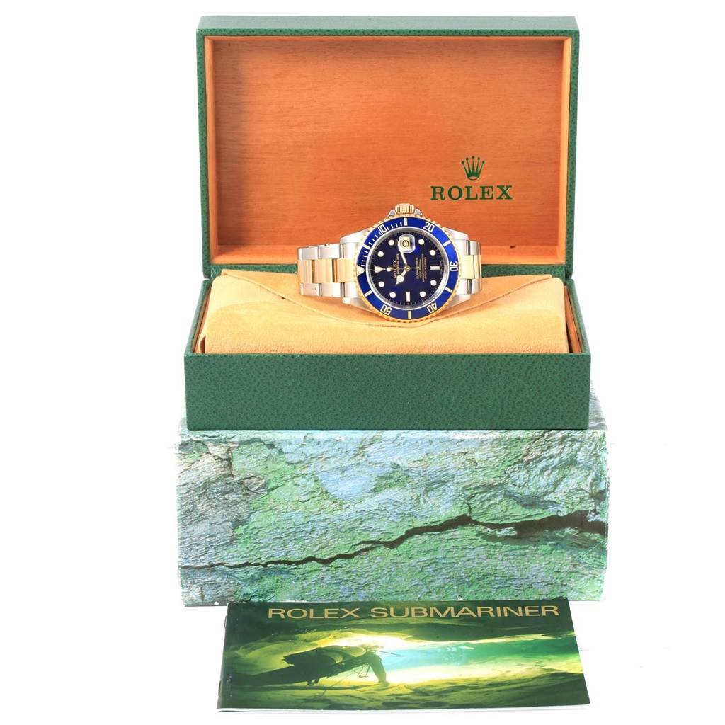 The Rolex Submariner 16613 Steel and Gold (two tone) Blue Dial 16613 Steel and Gold (two tone) Blue Dial watch is displayed front-on in an open box with its booklet in the foreground.