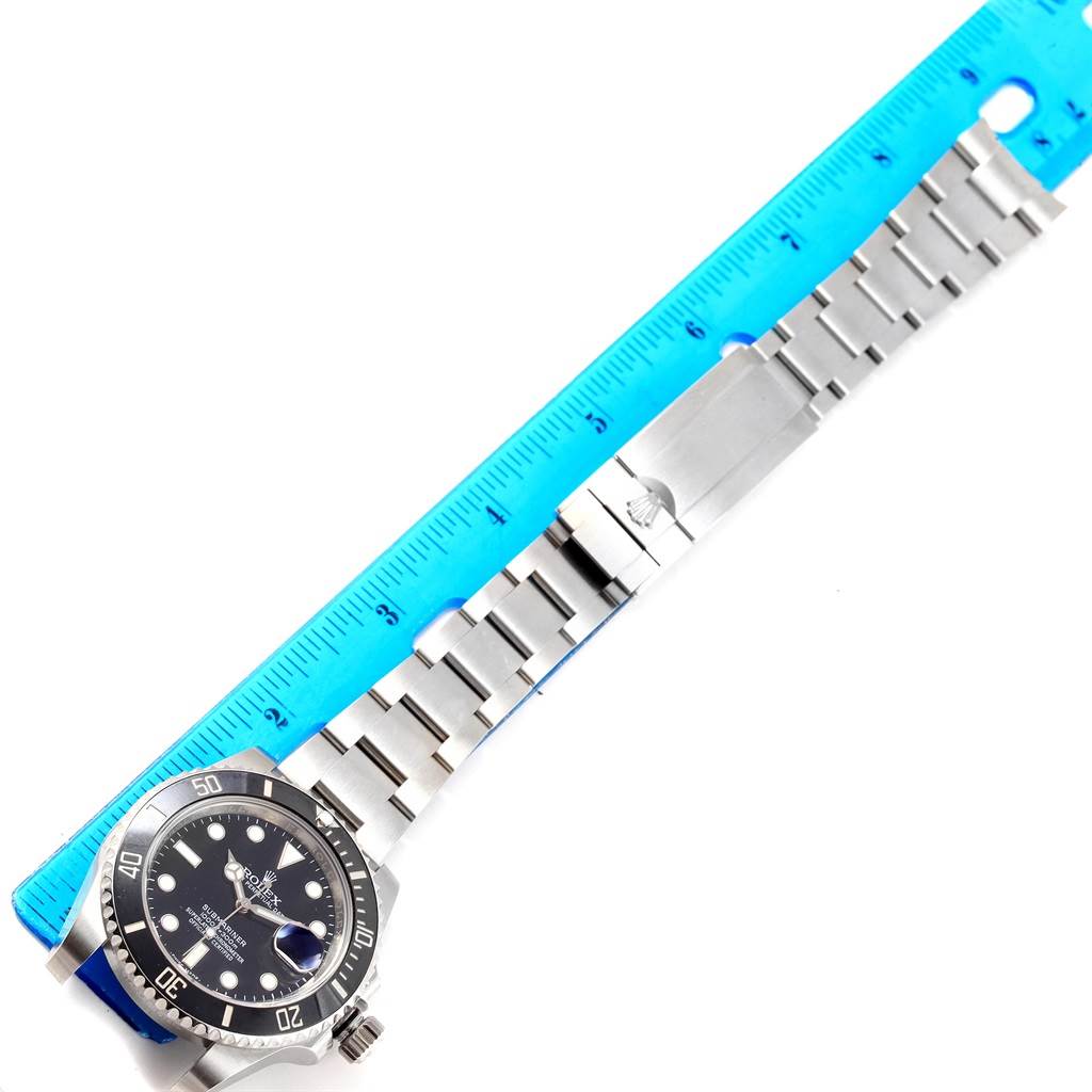 The image shows a top view of a Rolex Submariner 116610 Men's Stainless Steel Black Dial 116610 Men's Stainless Steel Black Dial watch and its metal band alongside a blue ruler.