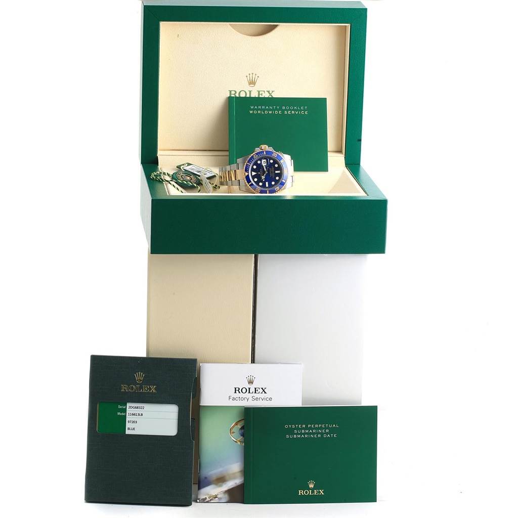 This image shows a Rolex Submariner 116613 Men's Steel and Gold (two tone) Blue Dial 116613 Men's Steel and Gold (two tone) Blue Dial watch positioned in an open box, surrounded by booklets and tags.