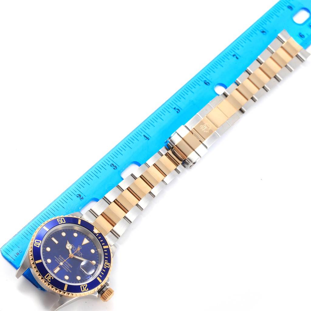 The Rolex Submariner 16613 Men's Steel and Gold (two tone) Blue Dial 16613 Men's Steel and Gold (two tone) Blue Dial watch is shown top-down next to a ruler, highlighting its stainless steel and gold bracelet and blue dial.