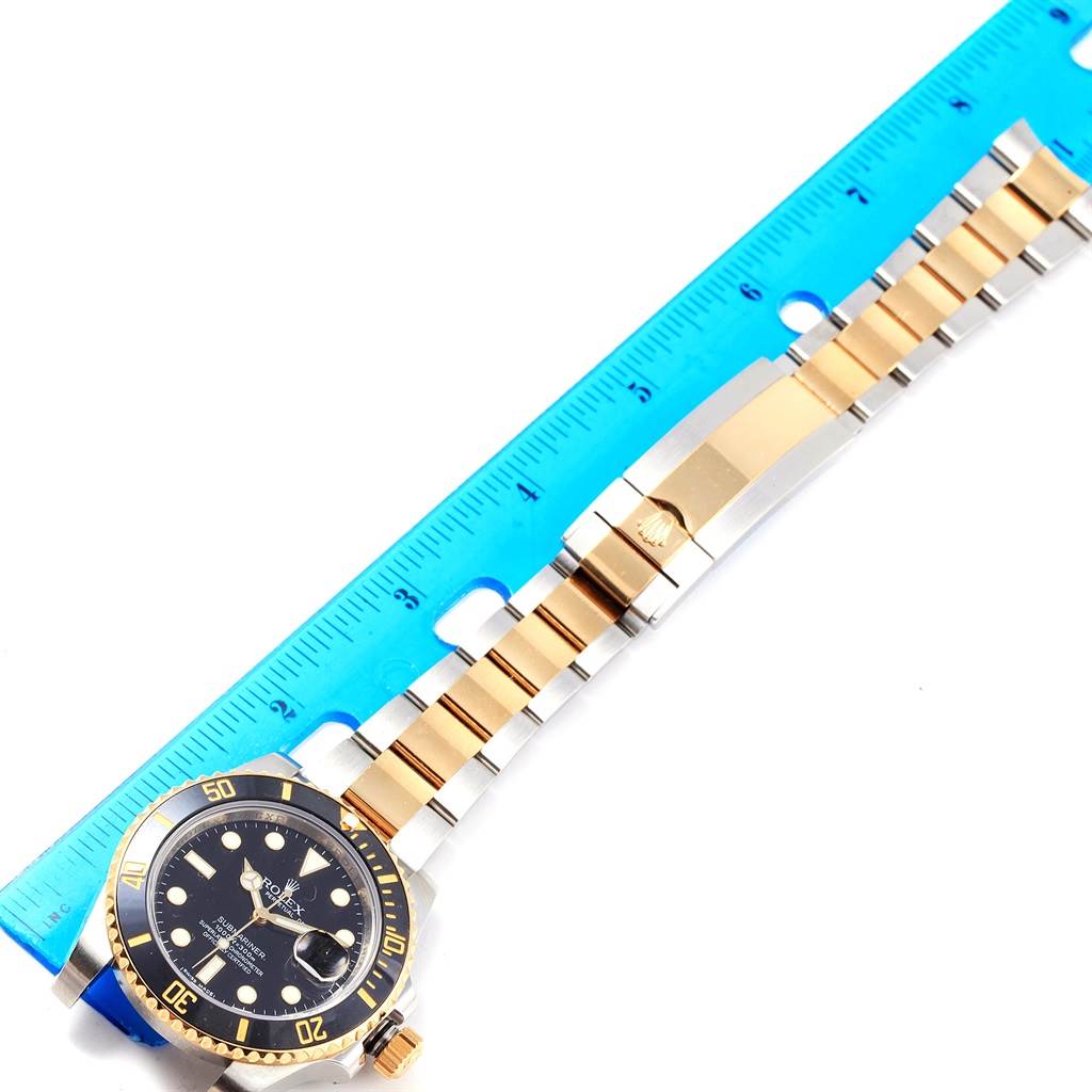 The image shows a Rolex Submariner 116613 Men's Steel and Gold (two tone) Black Dial 116613 Men's Steel and Gold (two tone) Black Dial watch in a top-down view, highlighting the face, bezel, and bracelet alongside a blue ruler.