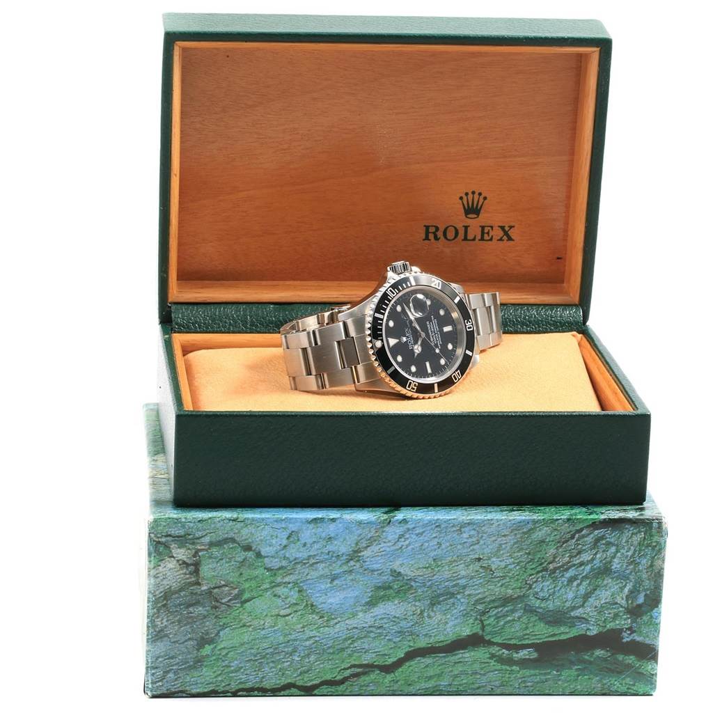 The Rolex Submariner 16610 Men
s Stainless Steel Black Dial 16610 Men
s Stainless Steel Black Dial watch is displayed at a slight angle within its open green and wood box.