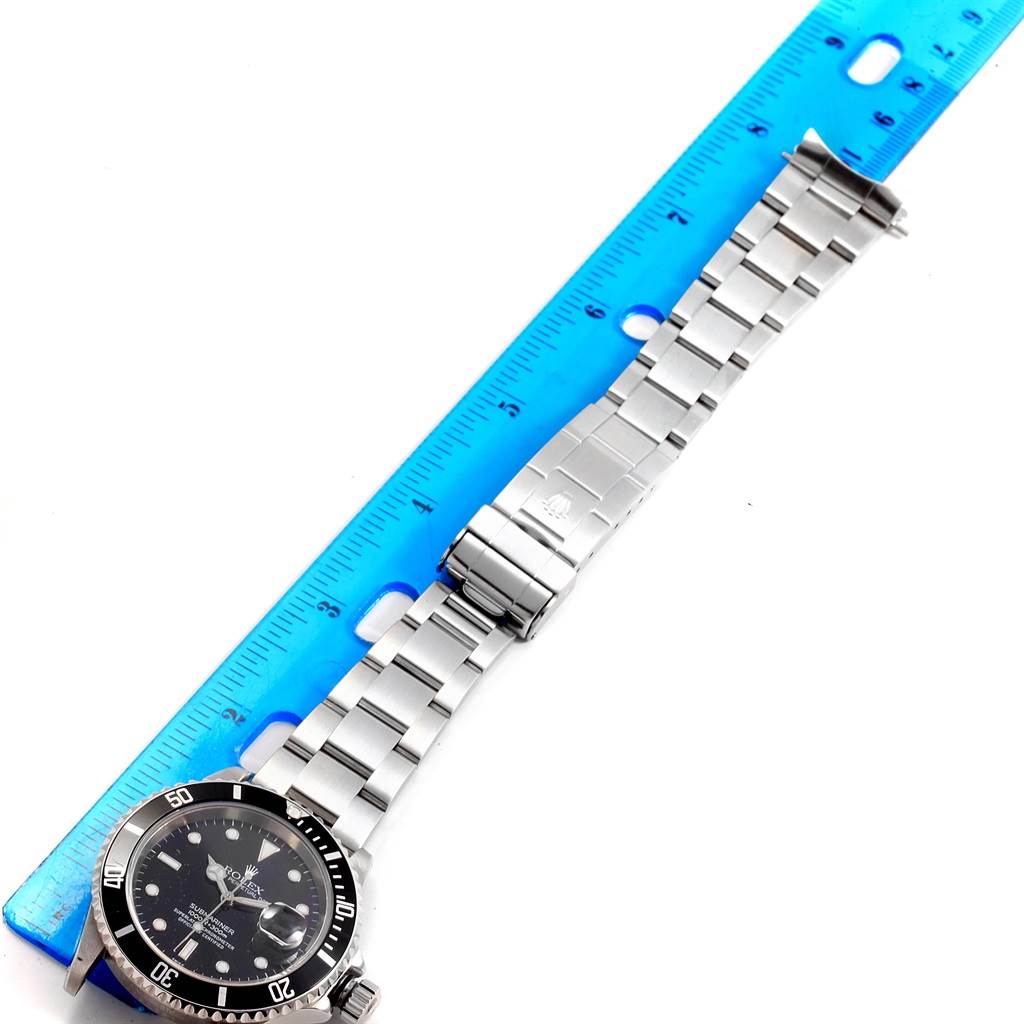 The image shows a Rolex Submariner 16610 Men
s Stainless Steel Black Dial 16610 Men
s Stainless Steel Black Dial watch lying flat with its band laid out next to a blue ruler.