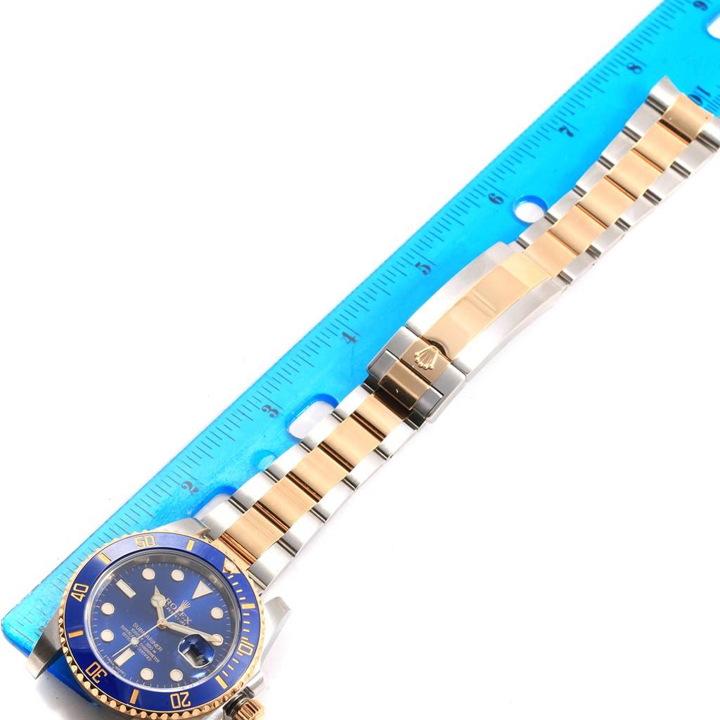 The image shows a flat-lay view of a Rolex Submariner 116613 Men's Steel and Gold (two tone) Blue Dial 116613 Men's Steel and Gold (two tone) Blue Dial watch with its blue dial, bezel, and two-tone bracelet, alongside a ruler.