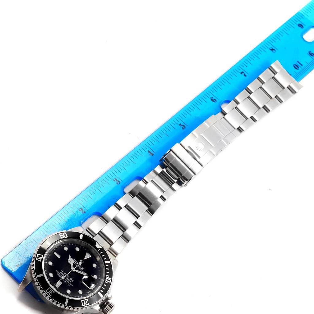 The image shows a Rolex Submariner 16610 Men
s Stainless Steel Black Dial 16610 Men
s Stainless Steel Black Dial watch fully extended next to a ruler, highlighting the face and bracelet.