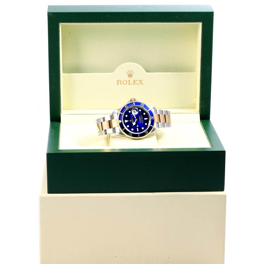 The Rolex Submariner 16613 Men
s Steel and Gold (two tone) Blue Dial 16613 Men
s Steel and Gold (two tone) Blue Dial watch is shown from the front, inside an open green and cream Rolex box.