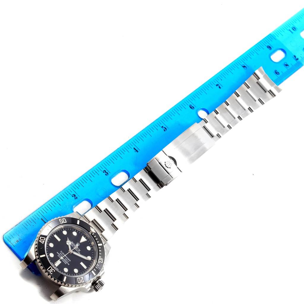 The image shows a Rolex Submariner 114060 Men
s Stainless Steel Black Dial 114060 Men
s Stainless Steel Black Dial watch at a top-down angle next to a ruler, displaying its face, bezel, and bracelet.